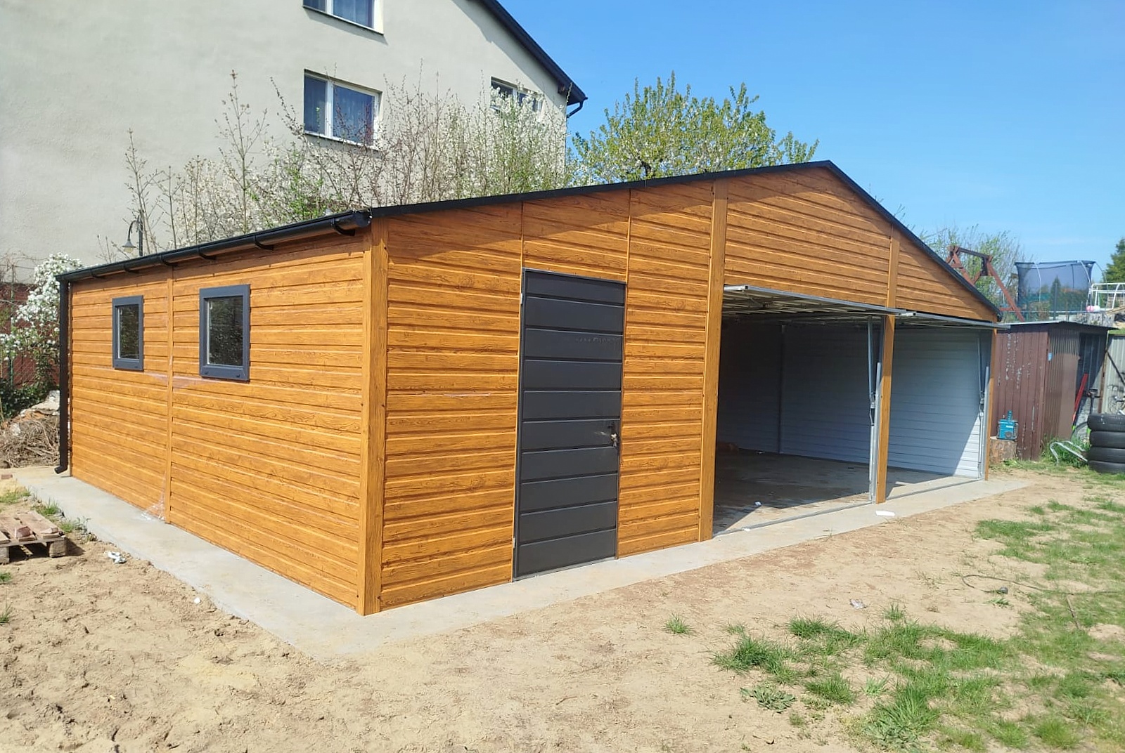 Garaż blaszany 9x6 - Trzystanowiskowy, Dach dwuspadowy, Kolor drewnopodobny złoty dąb, Bramy uchylne, Drzwi wejściowe Garaż blaszany 9x6 - Trzystanowiskowy, Dach dwuspadowy, Kolor drewnopodobny złoty dąb, Bramy uchylne, Drzwi wejściowe