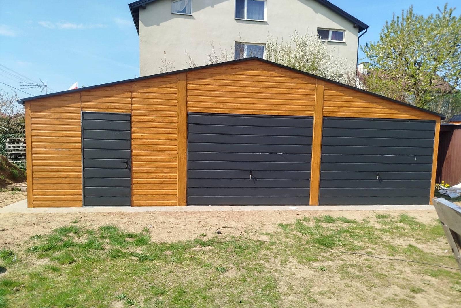 Garaż blaszany 9x6 - Trzystanowiskowy, Dach dwuspadowy, Kolor drewnopodobny złoty dąb, Bramy uchylne, Drzwi wejściowe Garaż blaszany 9x6 - Trzystanowiskowy, Dach dwuspadowy, Kolor drewnopodobny złoty dąb, Bramy uchylne, Drzwi wejściowe