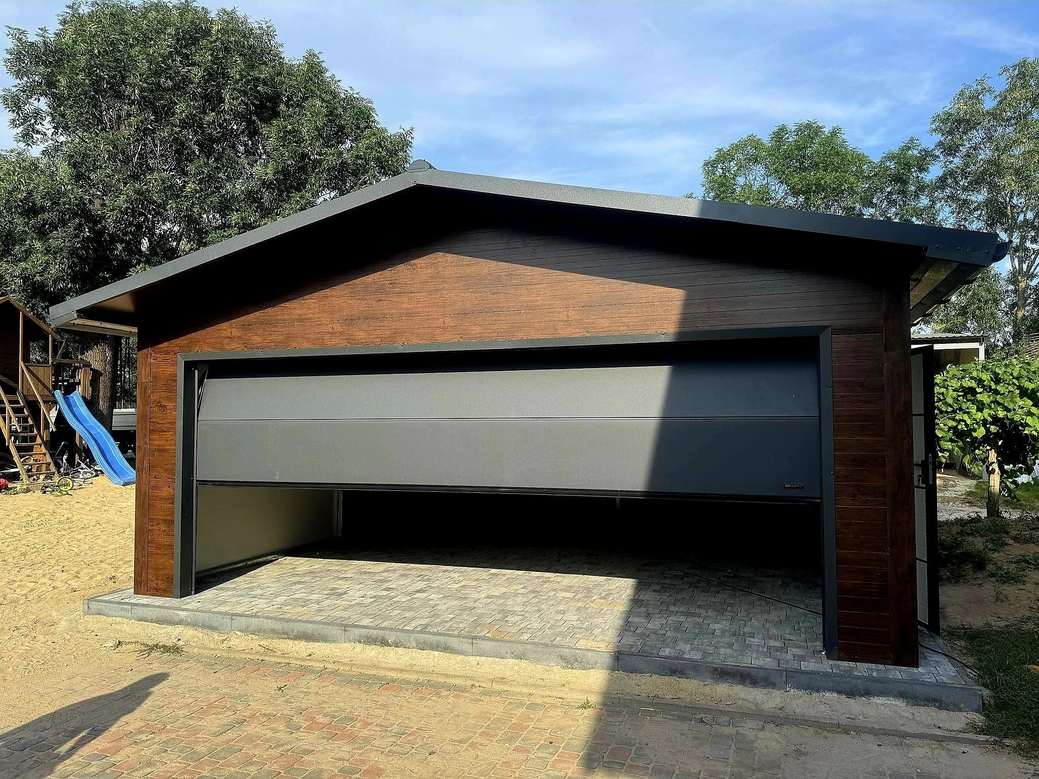 Garaż z płyty warstwowej 6x6 - Dach dwuspadowy, Ocieplany, Kolor drewnopodobny orzech, Brama segmentowa, Drzwi wejściowe Garaż z płyty warstwowej 6x6 - Dach dwuspadowy, Ocieplany, Kolor drewnopodobny orzech, Brama segmentowa, Drzwi wejściowe